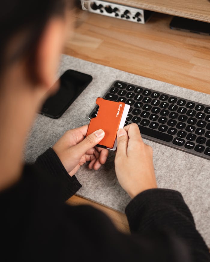 Close-up of hands holding a card wallet near a keyboard on a desk.